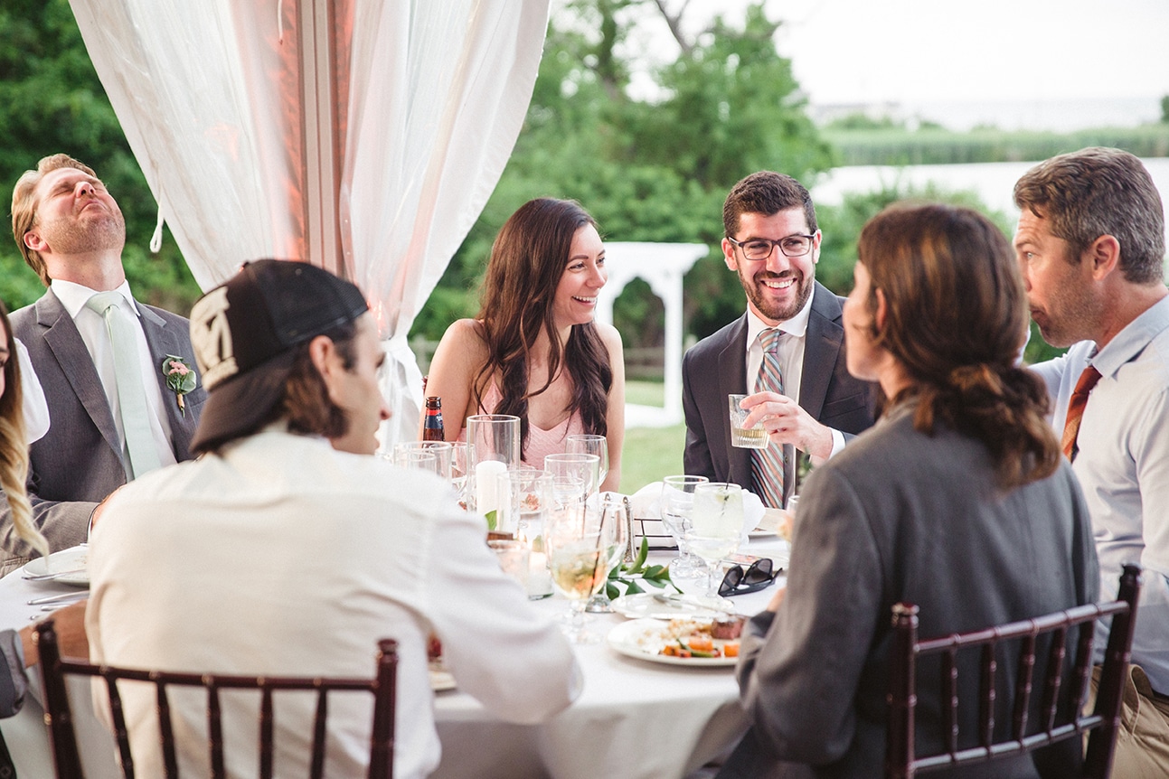 A documentary photograph of wedding guests talking and laughing at their table during a plimoth plantation wedding in plymouth, massachusetts