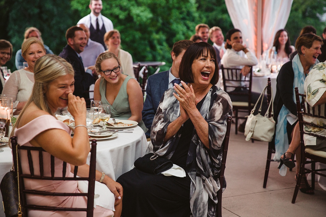 A documentary photograph of guests laughing during the toasts at a plimoth plantation wedding in plymouth, massachusetts
