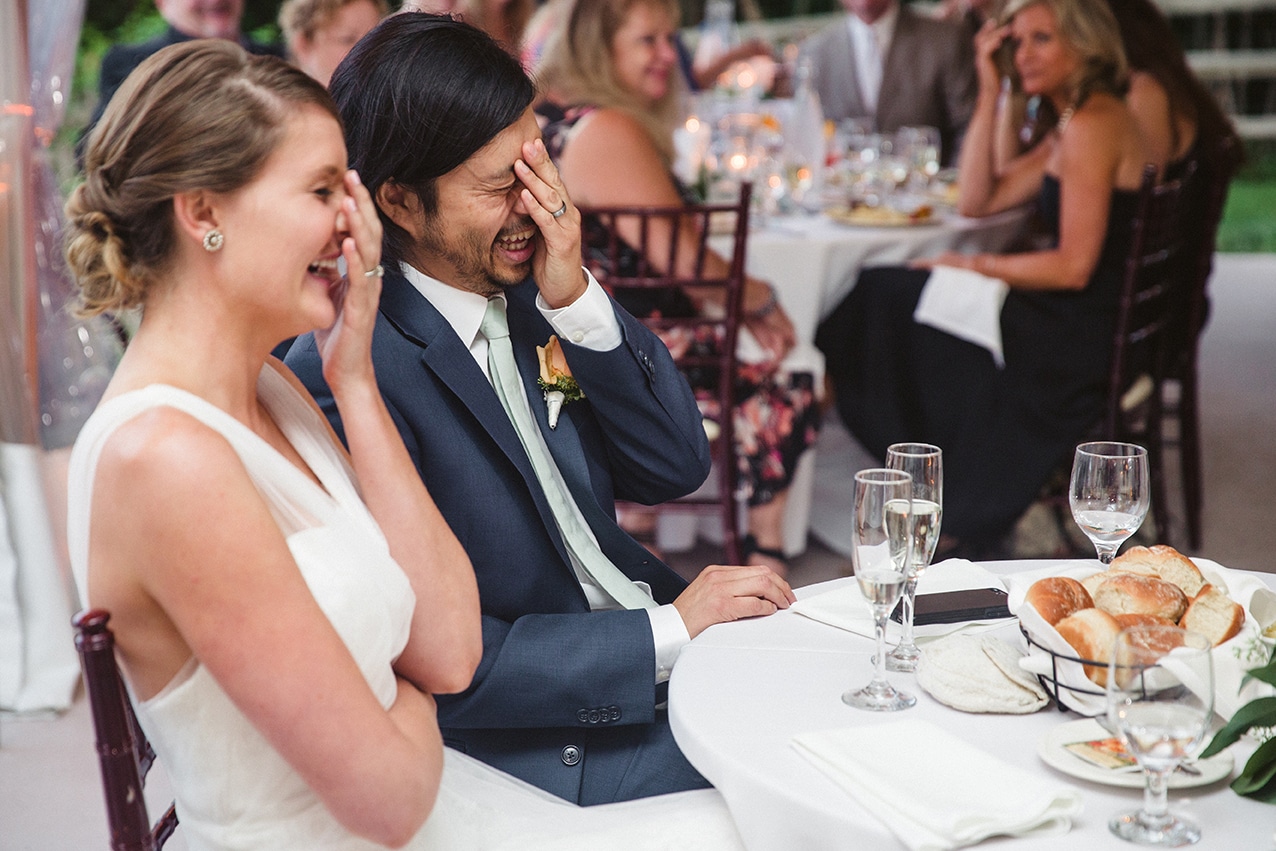 A documentary photograph of a bride and groom laughing and gesturing during the toasts at their plimoth plantation wedding in Plymouth, Massachusetts
