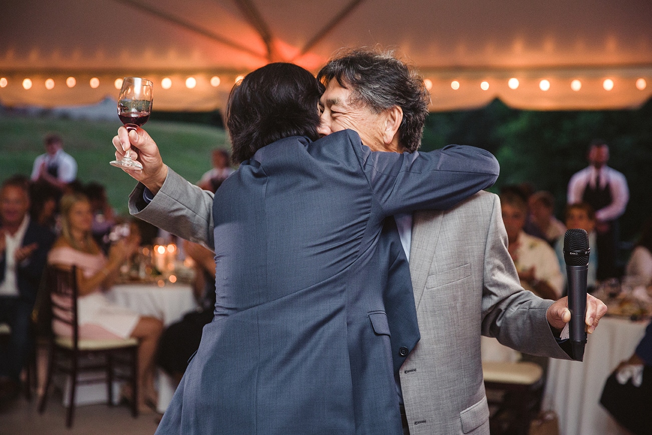 A documentary photograph of a groom hugging his father after the toast at this plimoth plantation wedding in plymouth, massachusetts