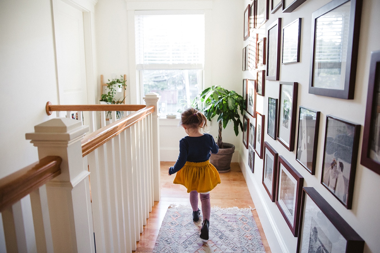 A documentary photograph of a little girl running in the hallway during an in home family lifestyle session in Boston, Massachusetts