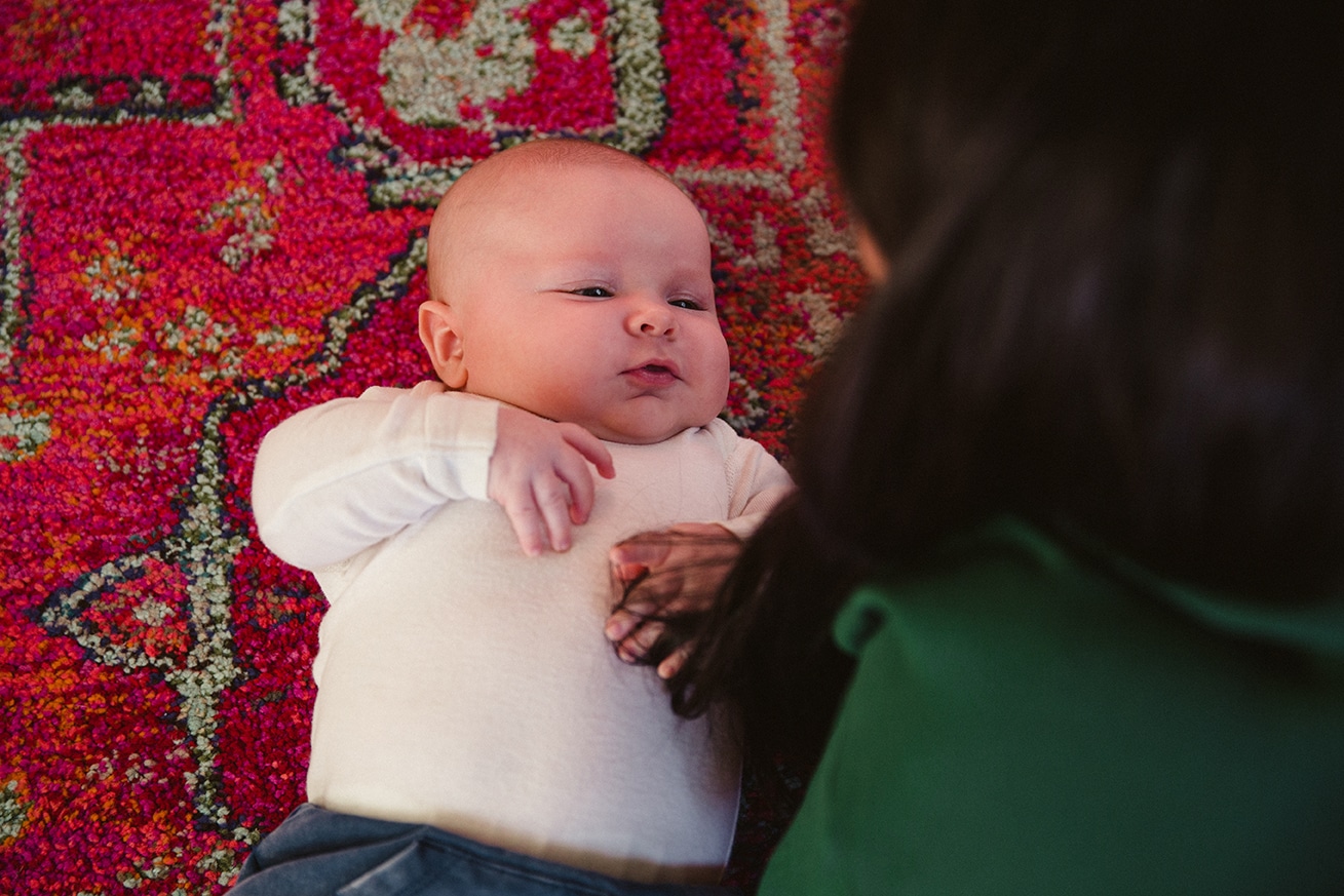 A documentary photograph of a baby boy looking up at his mom during an in home family lifestyle session in Boston, Massachusetts