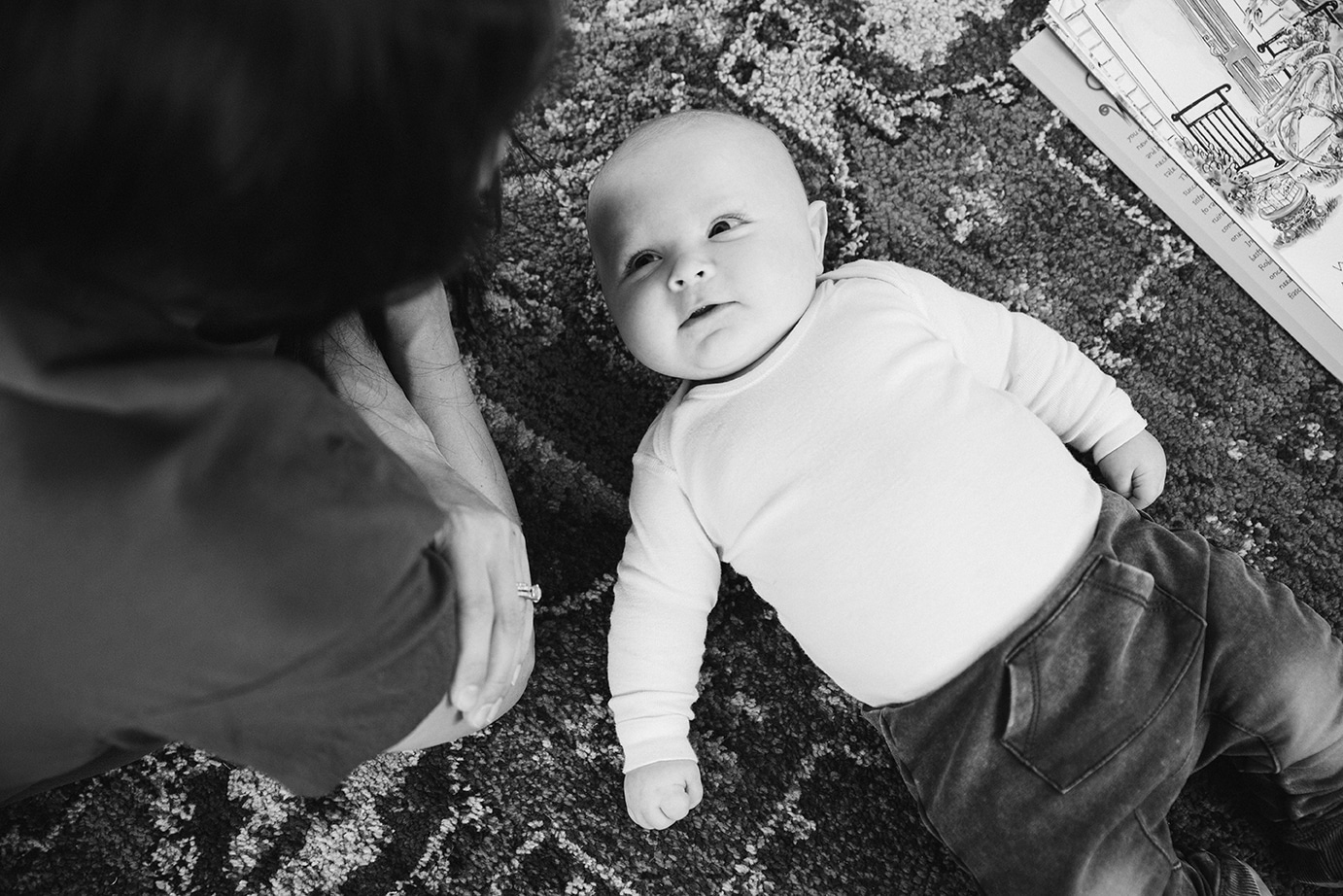 A documentary photograph of a baby looking up at his mom during their in home family lifestyle session in Boston, Massachusetts