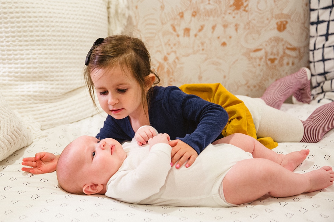 A documentary photograph of big sister cuddling with her baby brother during an in home family lifestyle session in Boston, Massachusetts