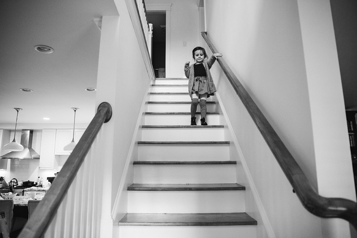 A documentary photograph of a little girl walking down the stairs during an in home family session in Boston, Massachusetts