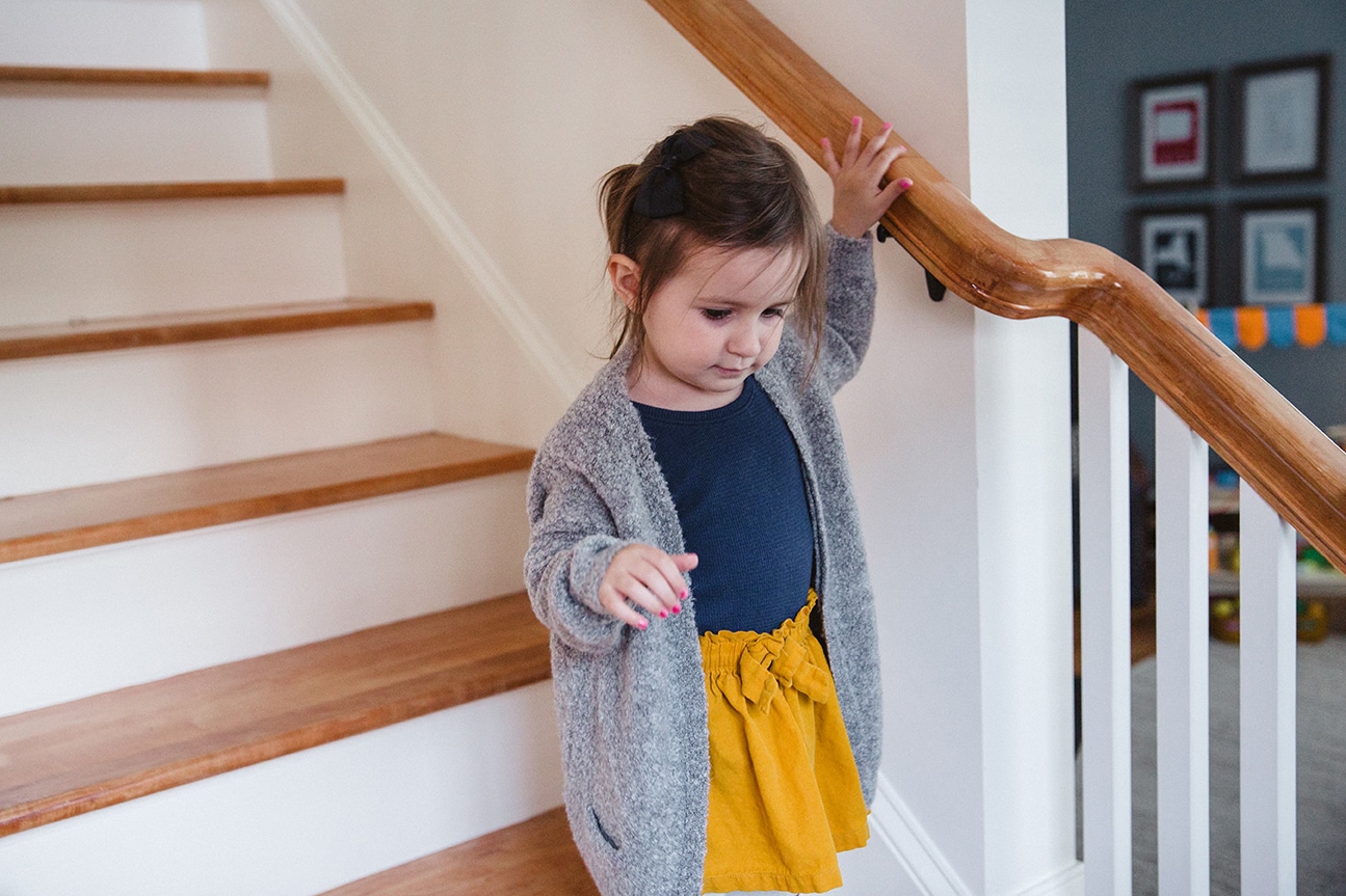 A documentary photograph of a little girl walking down the stairs during an in home family lifestyle session in Boston, Massachusetts