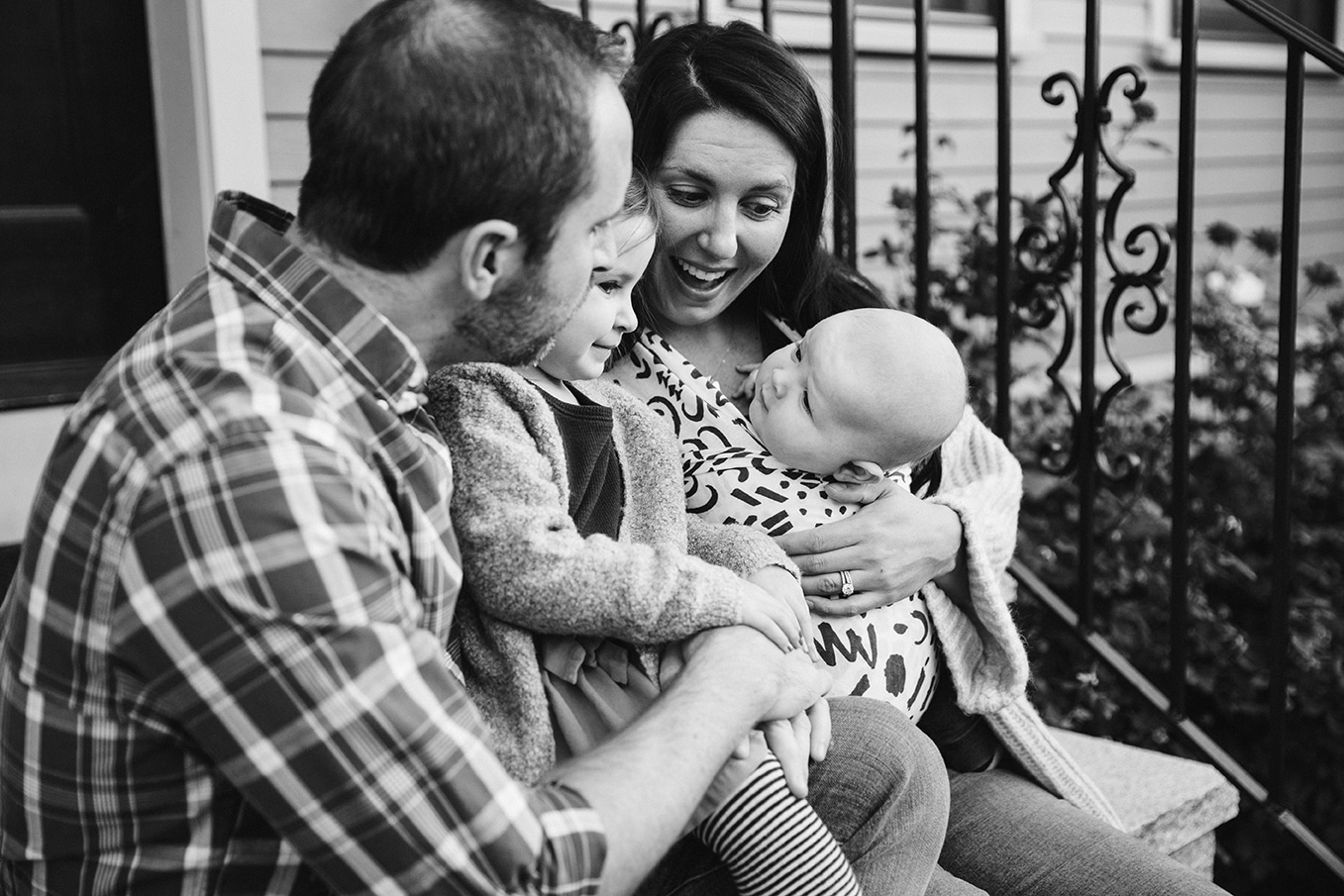 A documentary photograph of a family sitting on the porch together during their in home family lifestyle session in Boston, Massachusetts