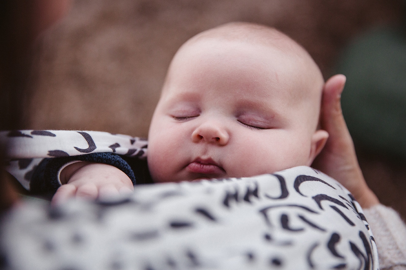 A documentary portrait of a sleeping baby boy being worn in a wrap during a family lifestyle session in Boston, Massachusetts