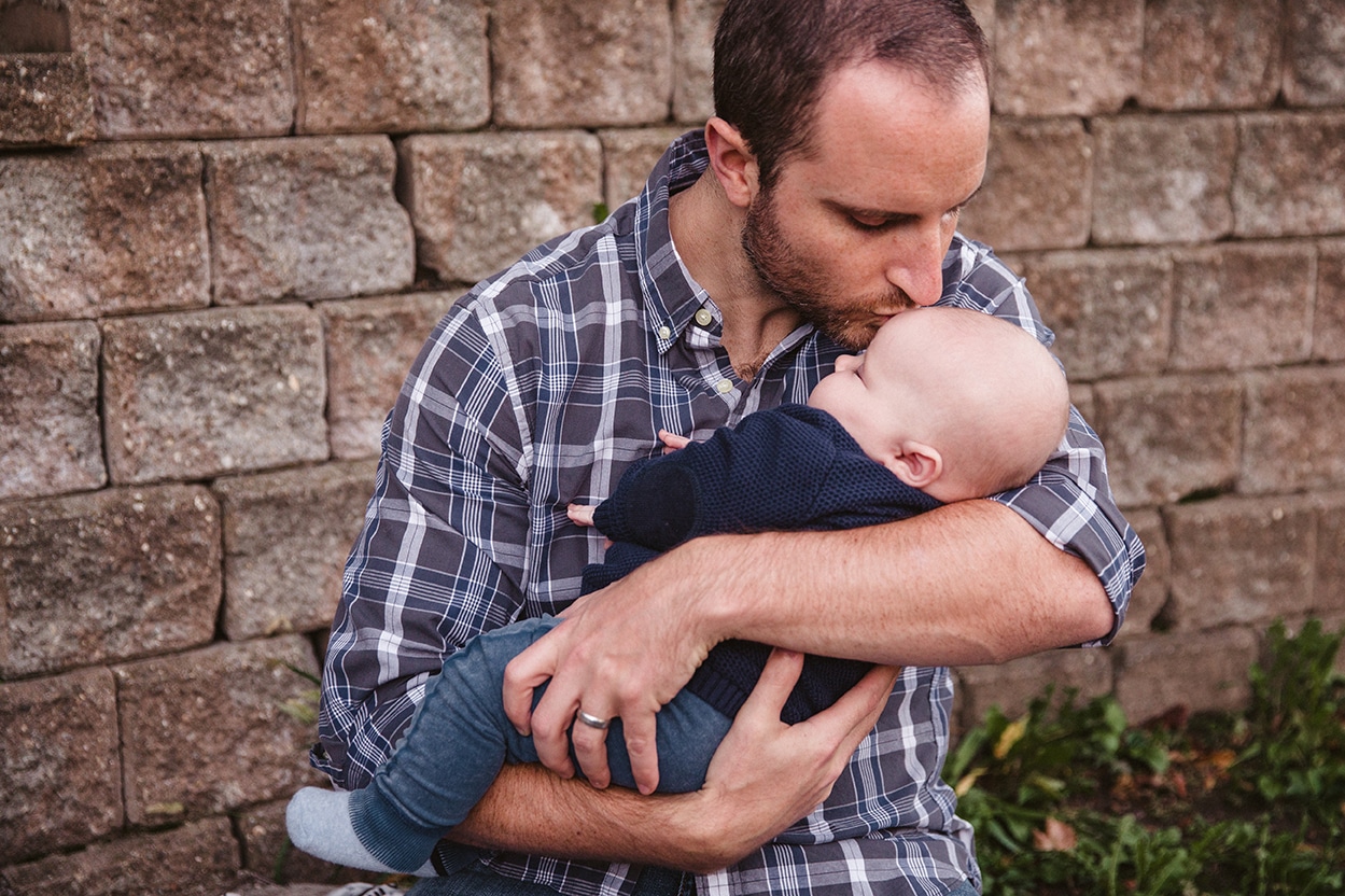 A documentary portrait of a dad kissing his baby boy during a family lifestyle session in Boston, Massachusetts
