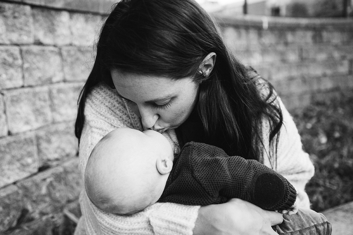 A documentary photograph of a mom kissing her baby boy at the playground during a family lifestyle session in Boston, Massachusetts
