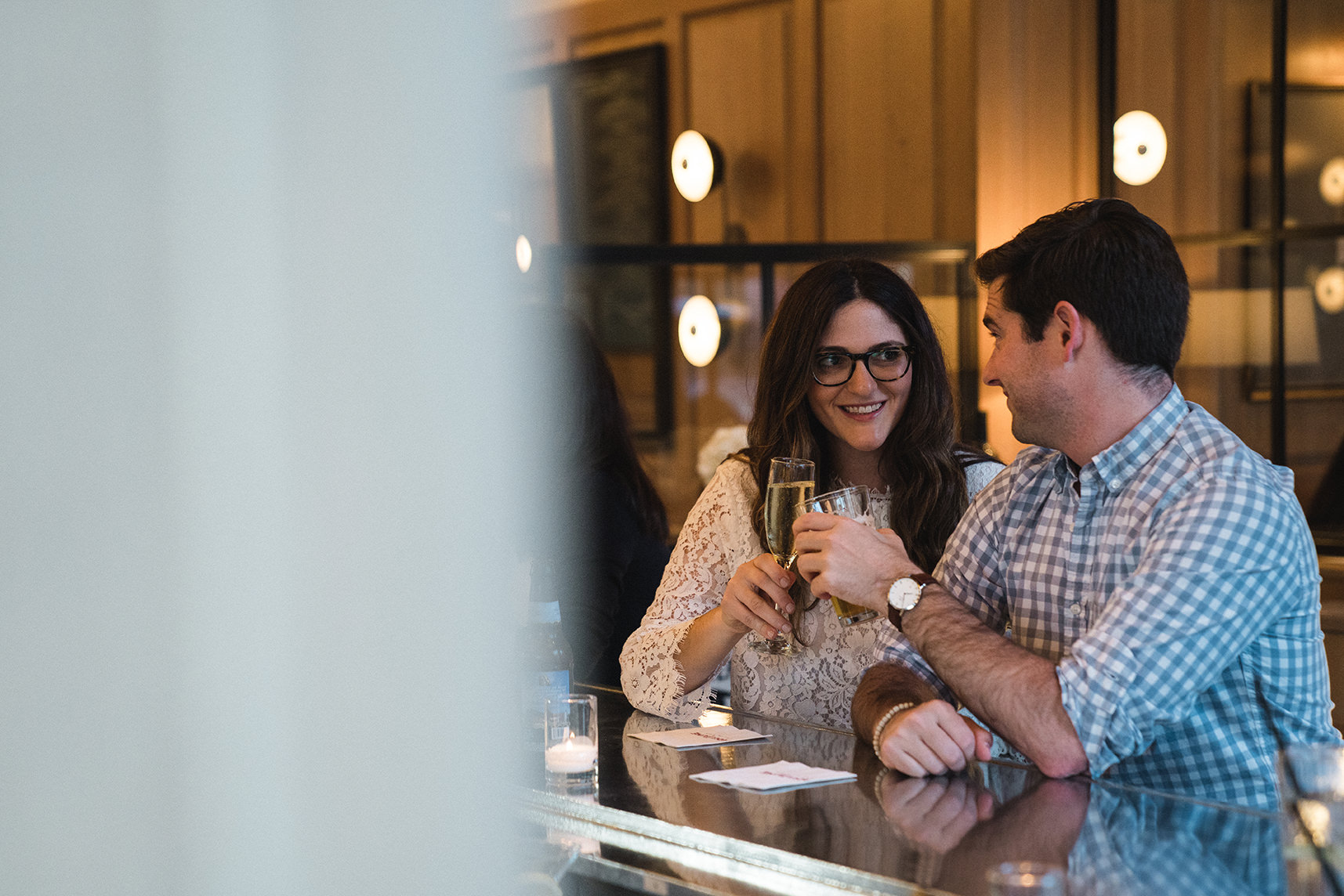 A documentary photograph of a couple sharing a celebratory drink at Aquitaine during their South End Boston Engagement Session
