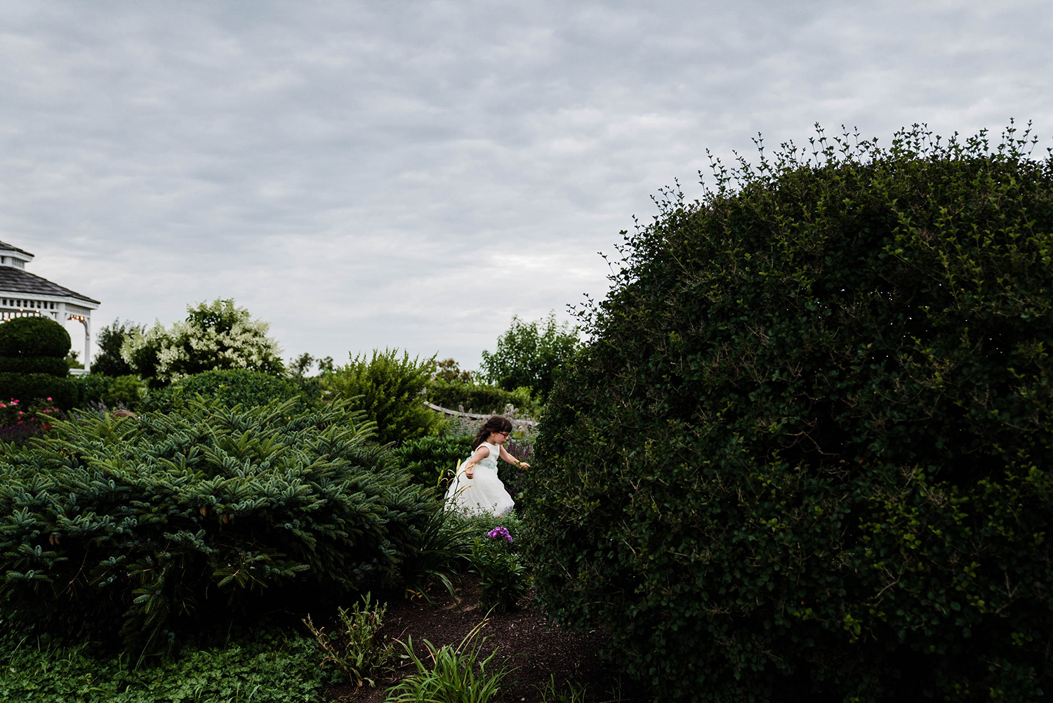 A documentary photograph of a flower girl running through the garden during an outdoor wedding outside of Boston
