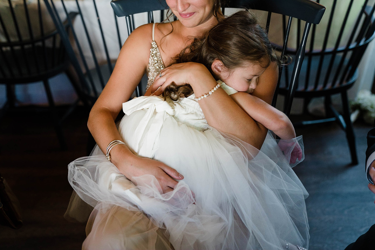 A documentary photograph of a flower girl sleeping in a bridesmaids lap during a Boston wedding reception at the Inn at Hastings Park