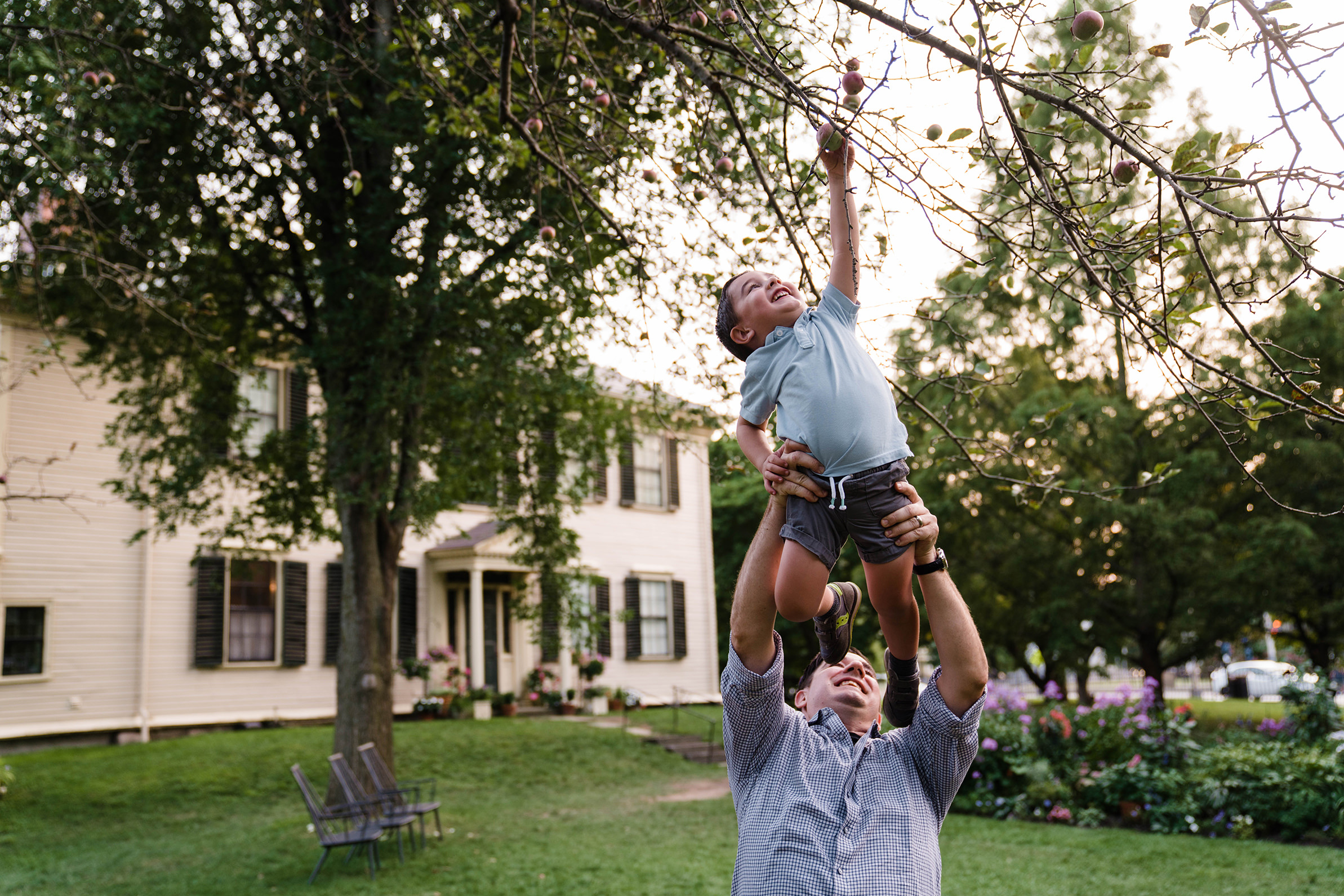 A best of Boston family photograph of father holding his son up to pick an apple off the tree during a lifestyle family session in Boston