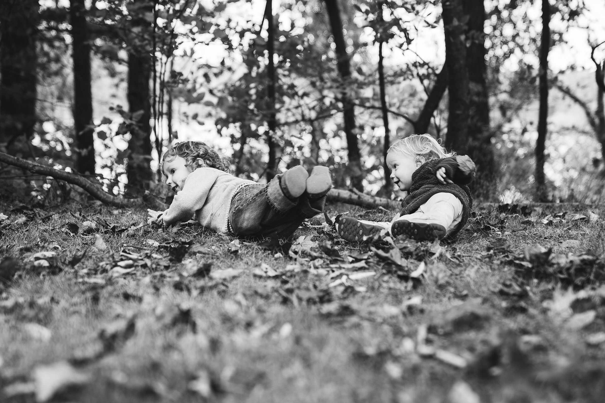 A best of Boston family photograph of a brother and sister rolling in the leaves during their lifestyle family session at Jamaica pond in Boston