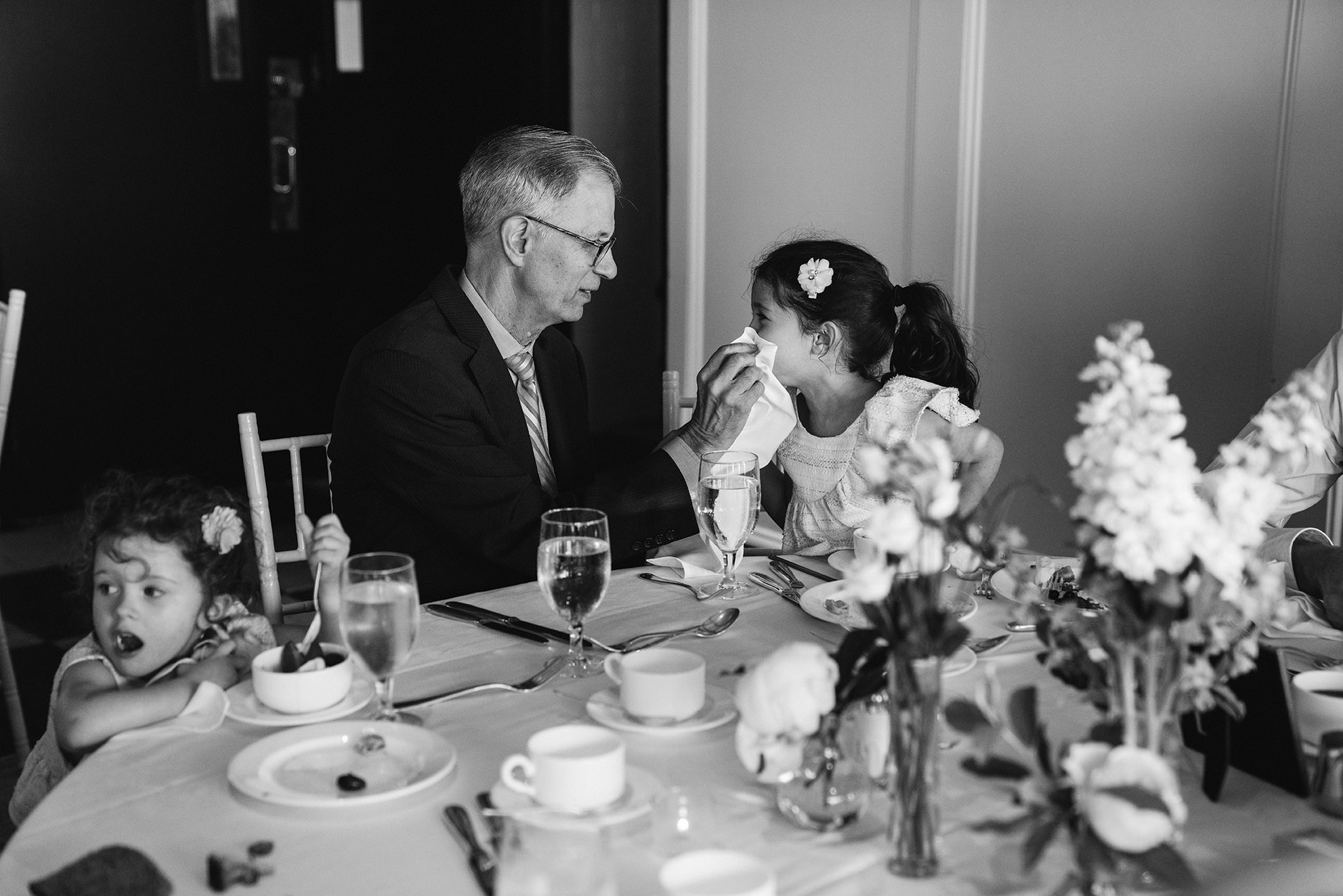 A best of Boston wedding photograph of a grandfather wiping his granddaughter's face during a Taj Boston Rooftop wedding reception in Boston