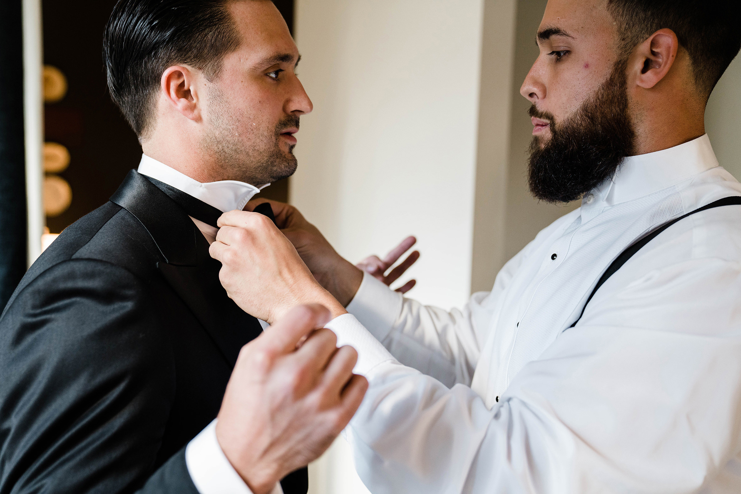 A best of Boston wedding photograph of groomsmen helping a groom with his bowtie before his State Room wedding
