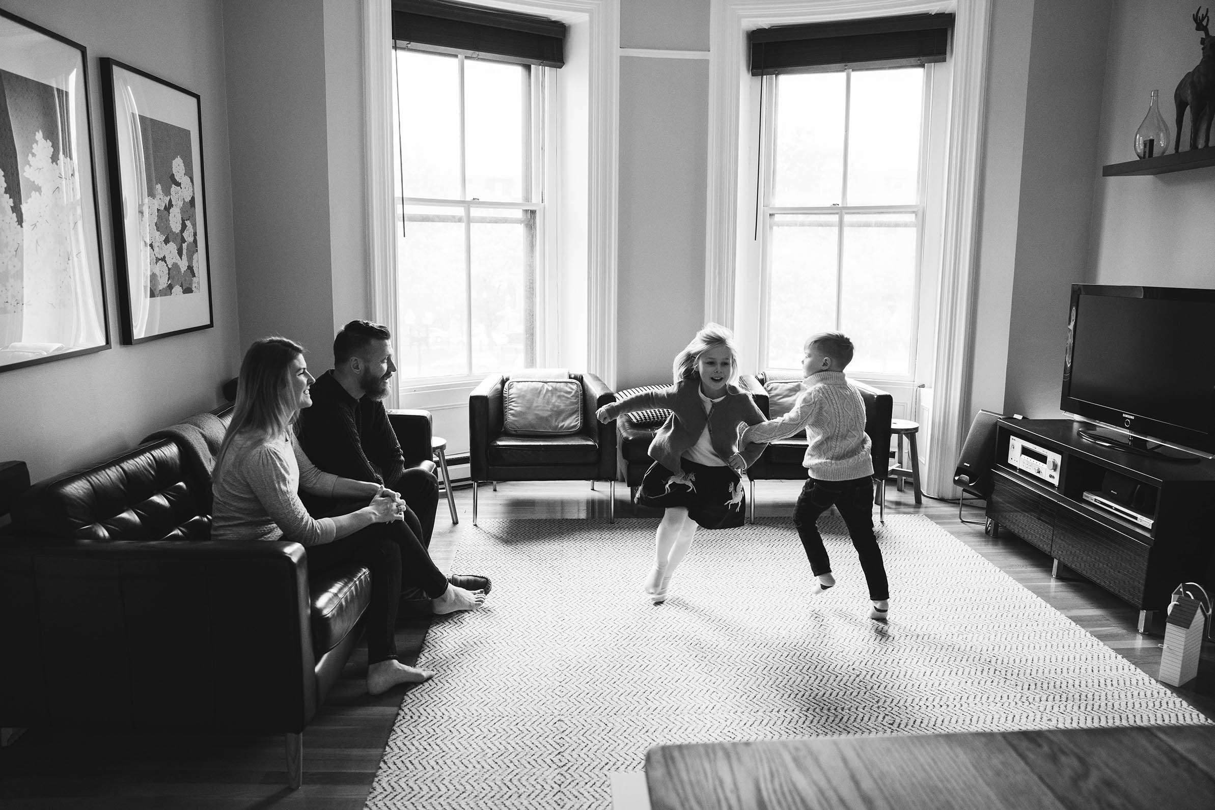A documentary photograph of a two kids dancing in the living room during their in home family session in Boston's South End