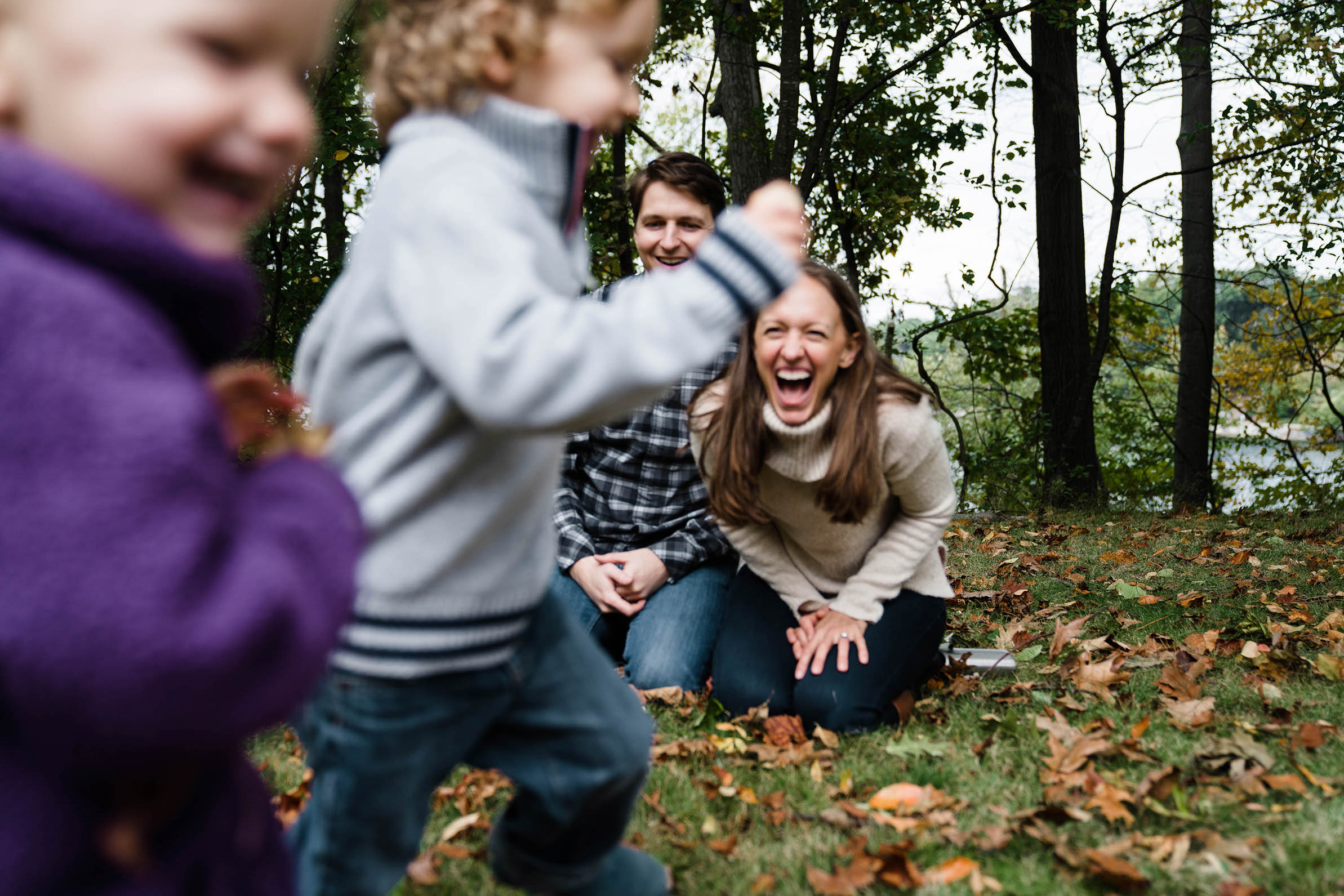A documentary photograph of a mom and dad laughing as their kids run around during their family session at Jamaica Pond in Boston