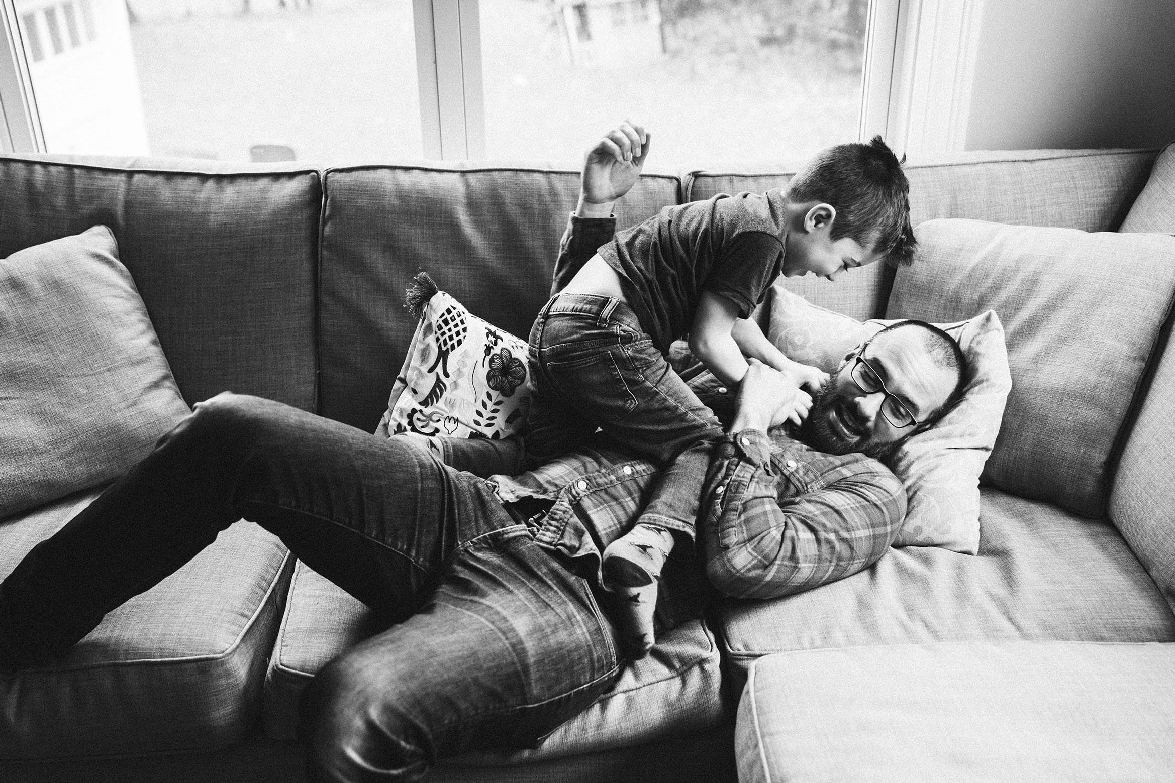 A documentary photograph of a father and son playing on the couch during an in home family session in Boston