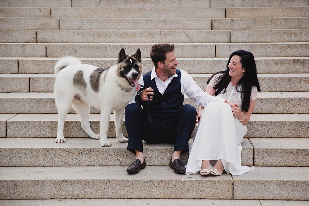 A documentary photograph of a couple laughing together as they sit on the steps of Boston Common with their during their Boston Engagement Session