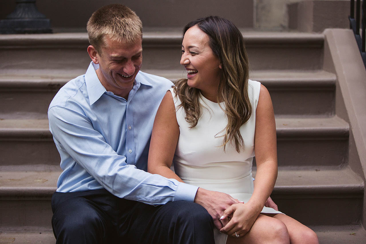 A documentary photograph of a couple laughing together on the steps of their Back Bay home during their Boston engagement session