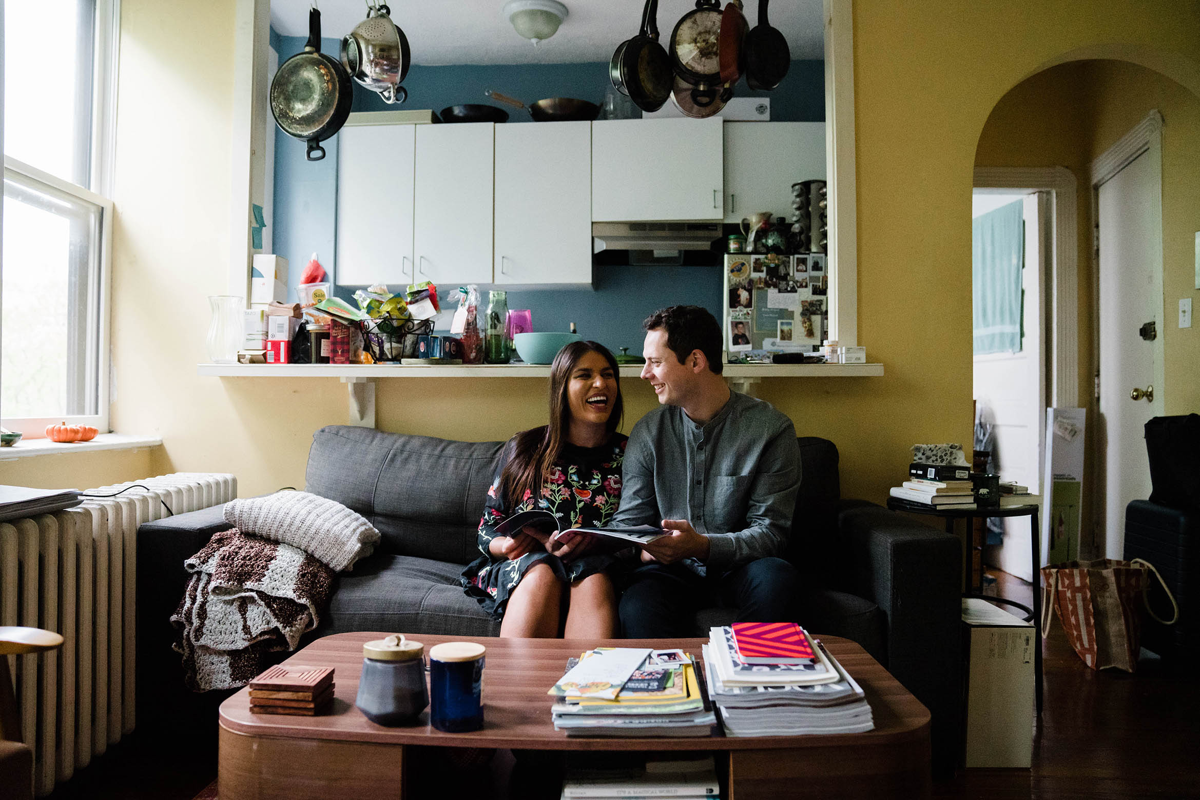 A documentary photograph of a couple laughing together on their couch during an in home Boston engagement session in Beacon Hill