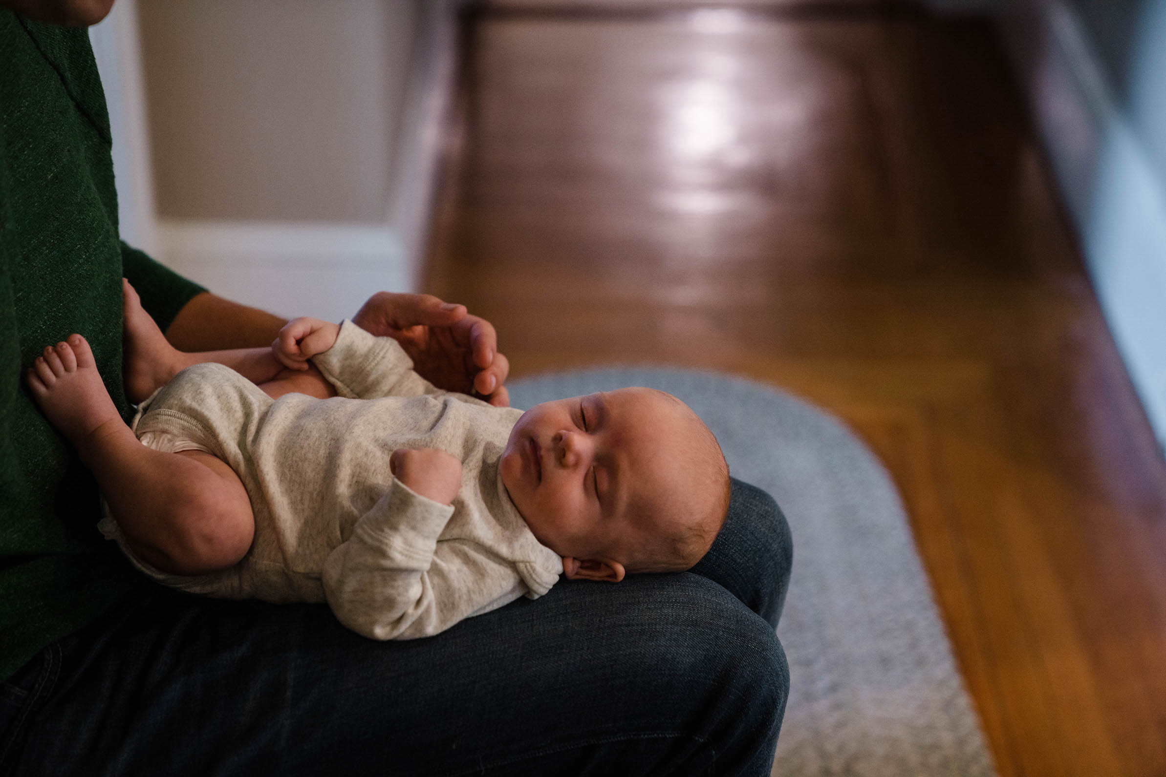 A documentary photograph of a baby sleeping on his father's lap during an in home family session in Boston