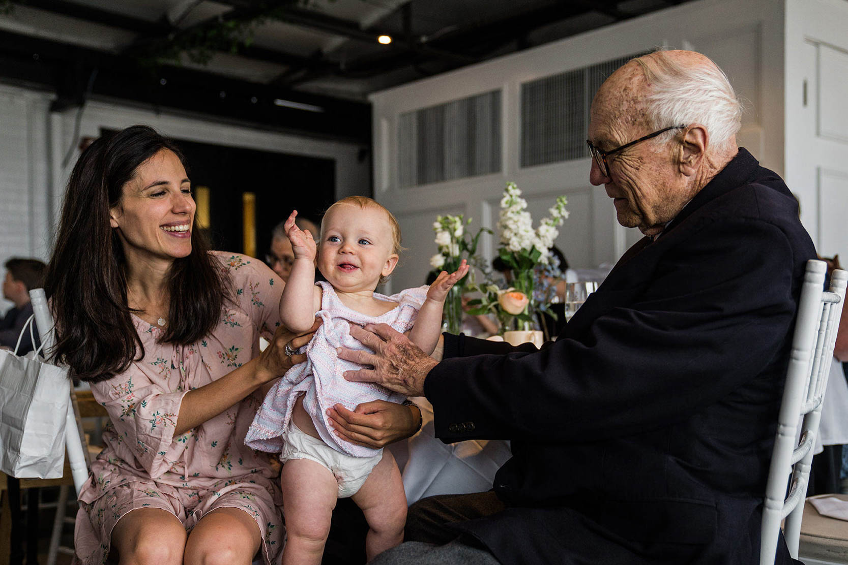A documentary photograph of a mother, baby and grandfather hanging out during a Taj Boston Wedding reception