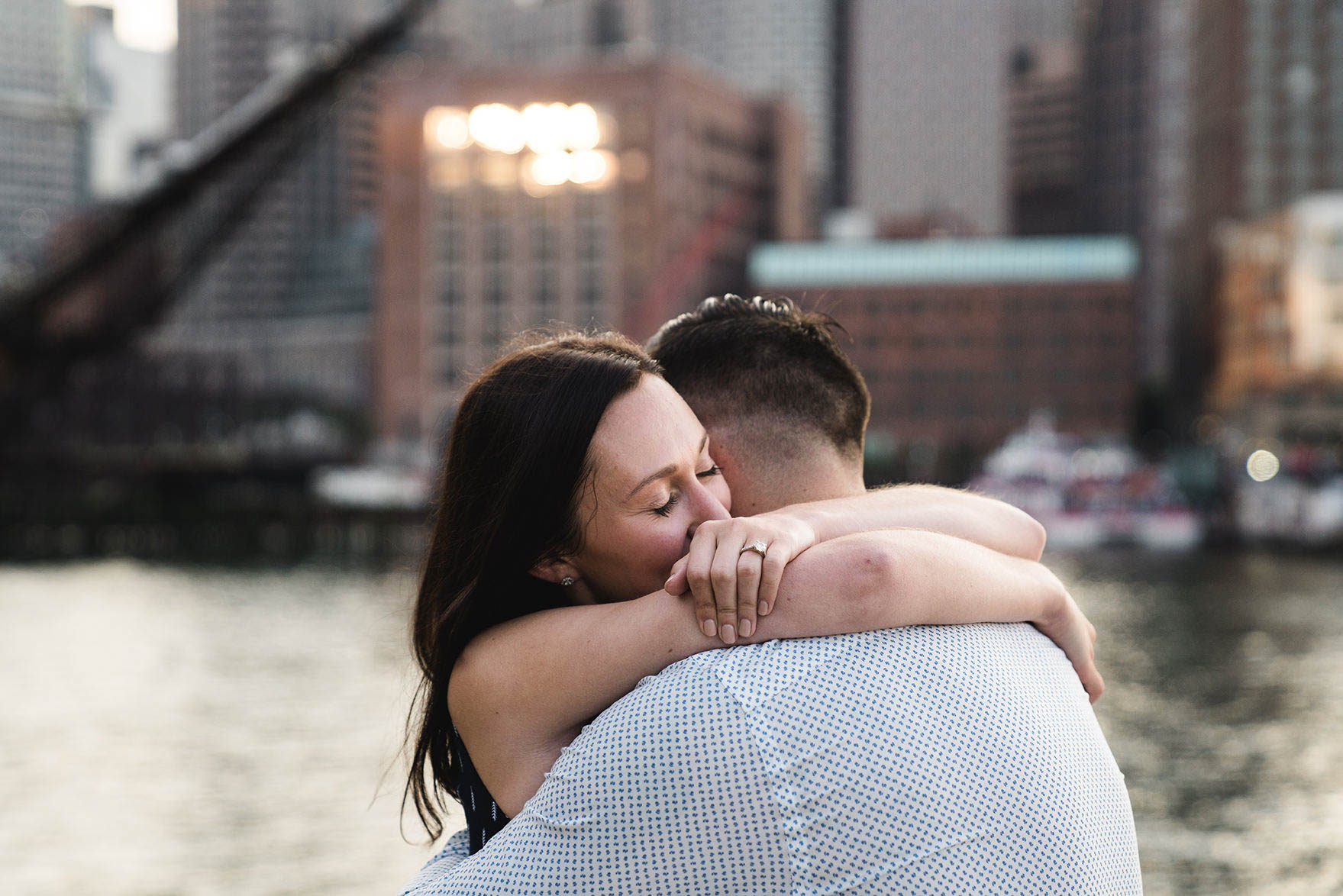 A documentary portrait of a couple hugging during their Boston engagement session at Fan Pier