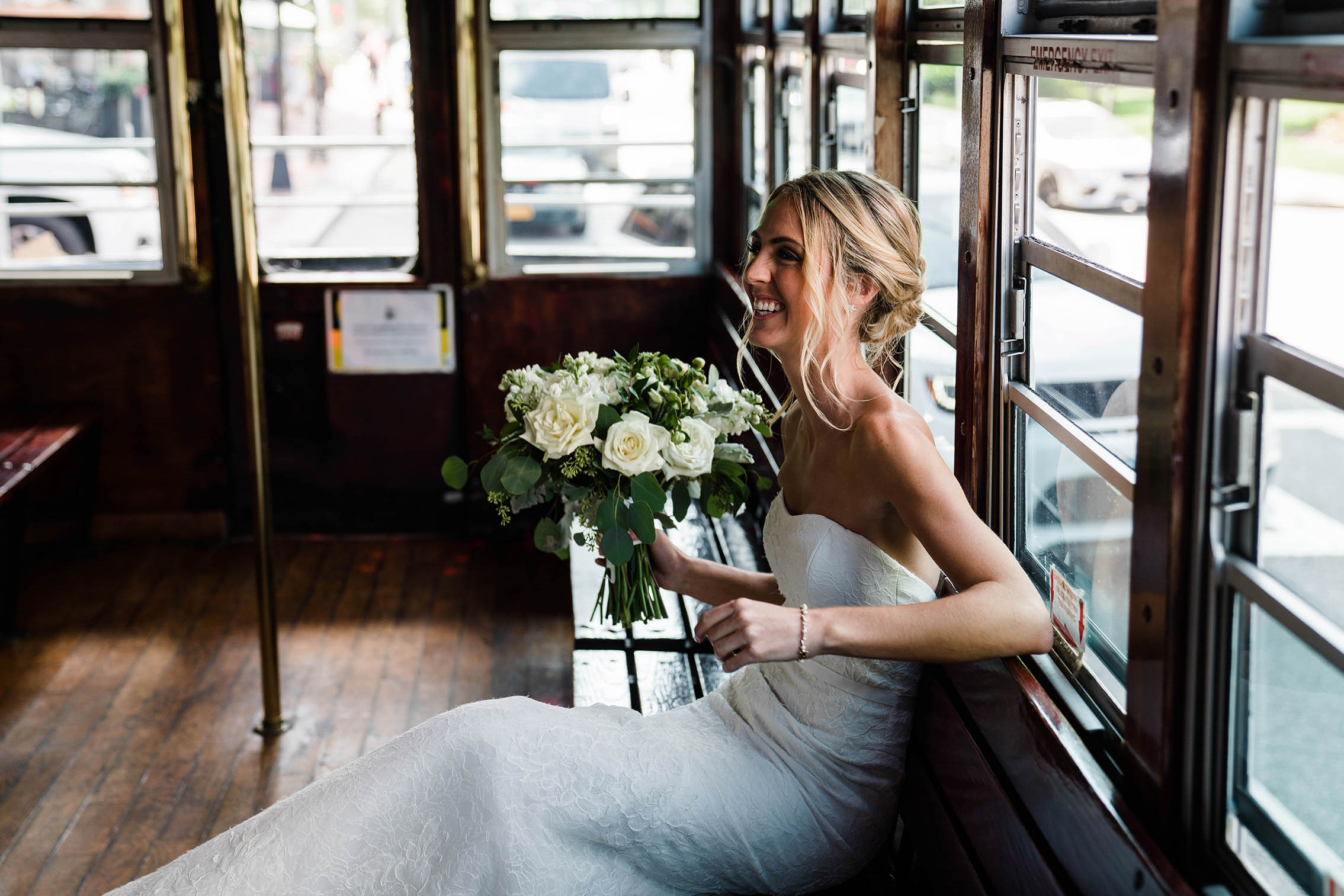A documentary photograph of bride laughing while she waits for her groom to join her on the trolley during their Boston Wedding