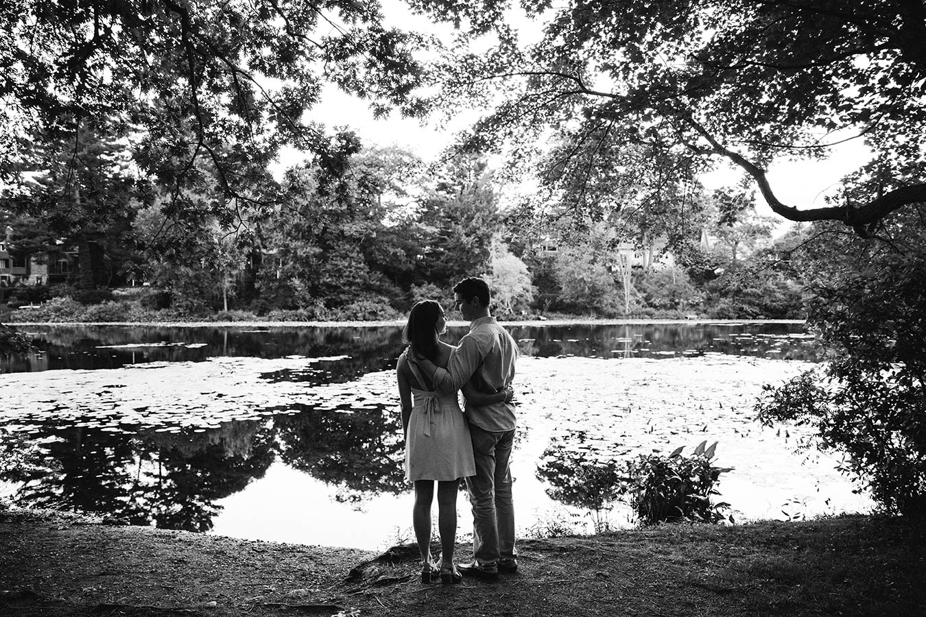 A documentary engagement session of a couple hugging and looking out at the water during their Boston engagement session at Auburndale Cove
