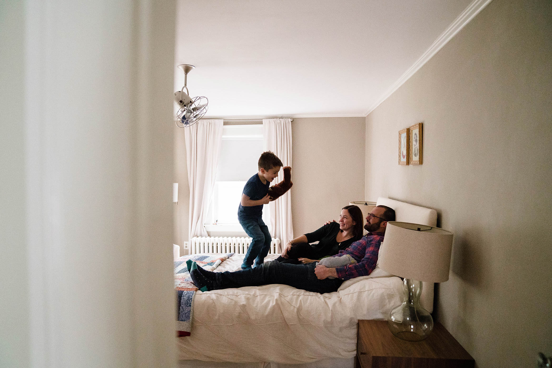 A documentary photograph of a boy jumping on the bed with his parents during an in home family session in Boston