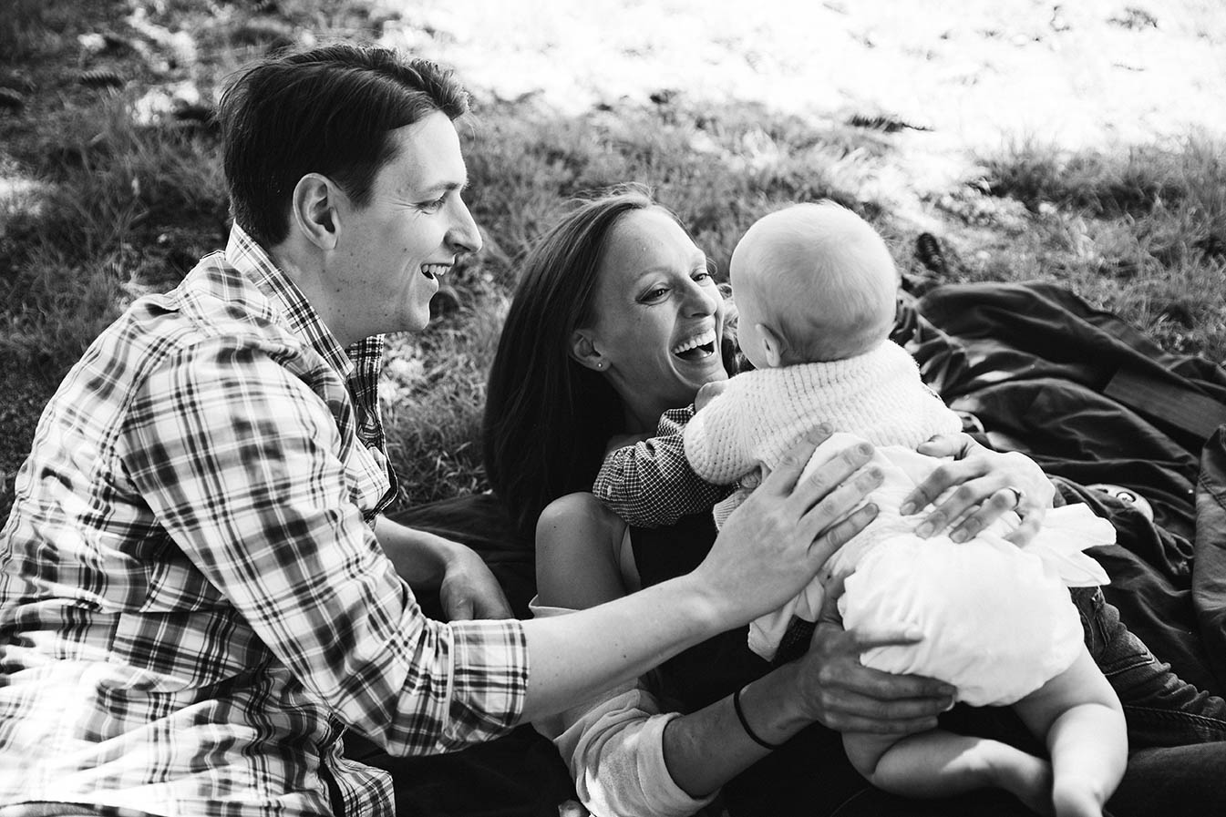 A documentary photograph of a parents snuggling their baby at the park during their Boston family session