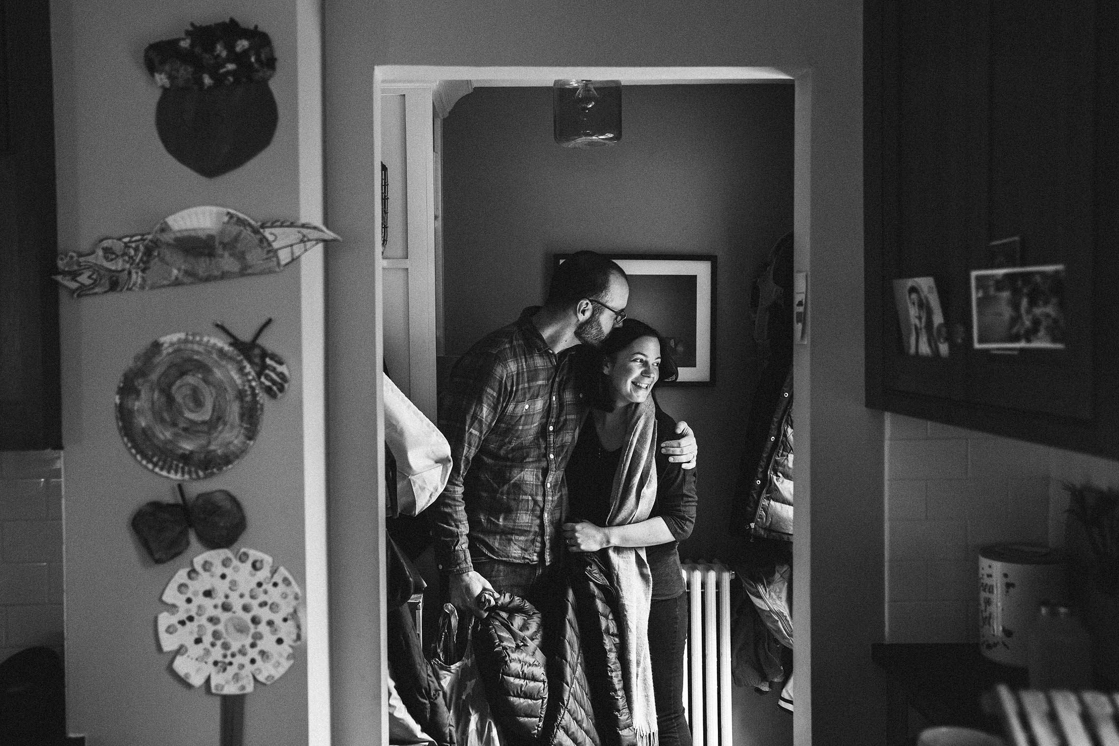 A documentary photograph of parents giving each other a kiss as they put on the coats and leave the house during a Boston family session