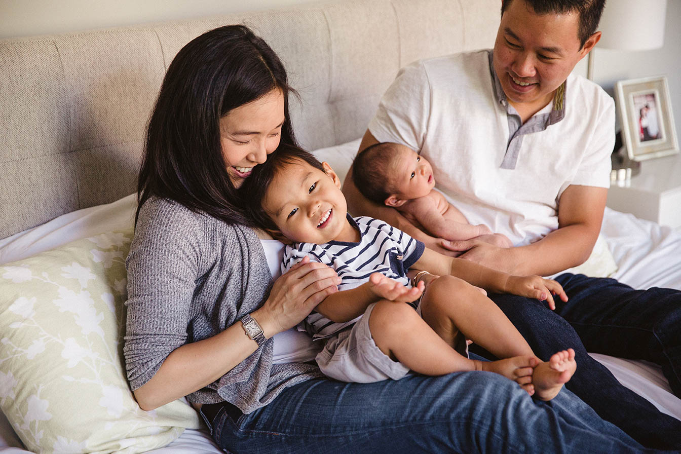 A documentary photograph of a family snuggling and laughing in bed during an in home newborn family session in Boston's Jamaica Plain