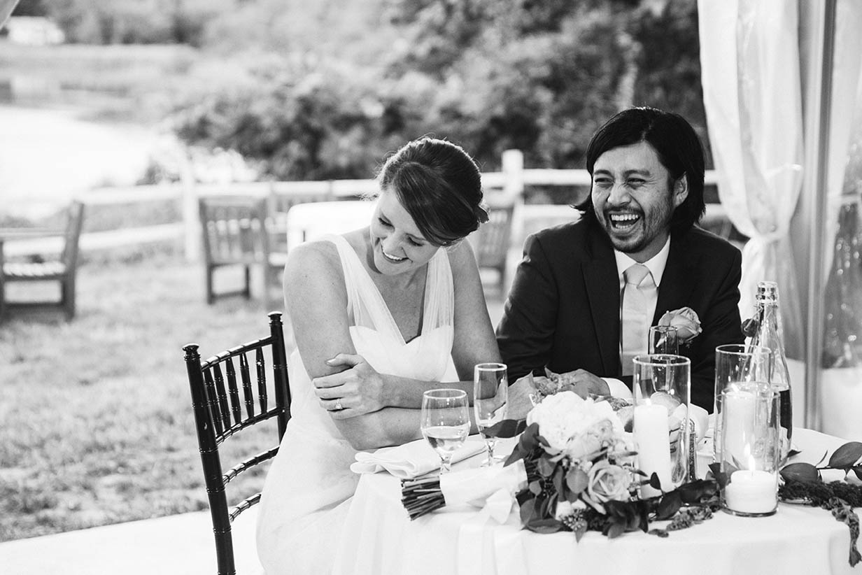 A documentary photograph of a bride and groom laughing during the wedding speeches at their Boston wedding