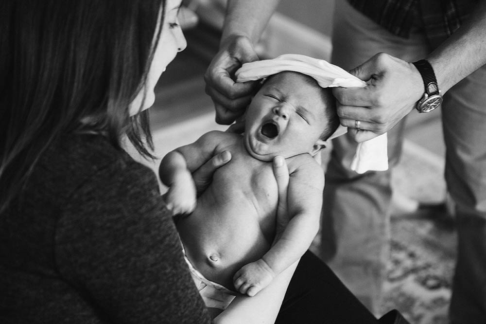 A documentary photograph of parents dressing their baby during an in home newborn session outside of Boston