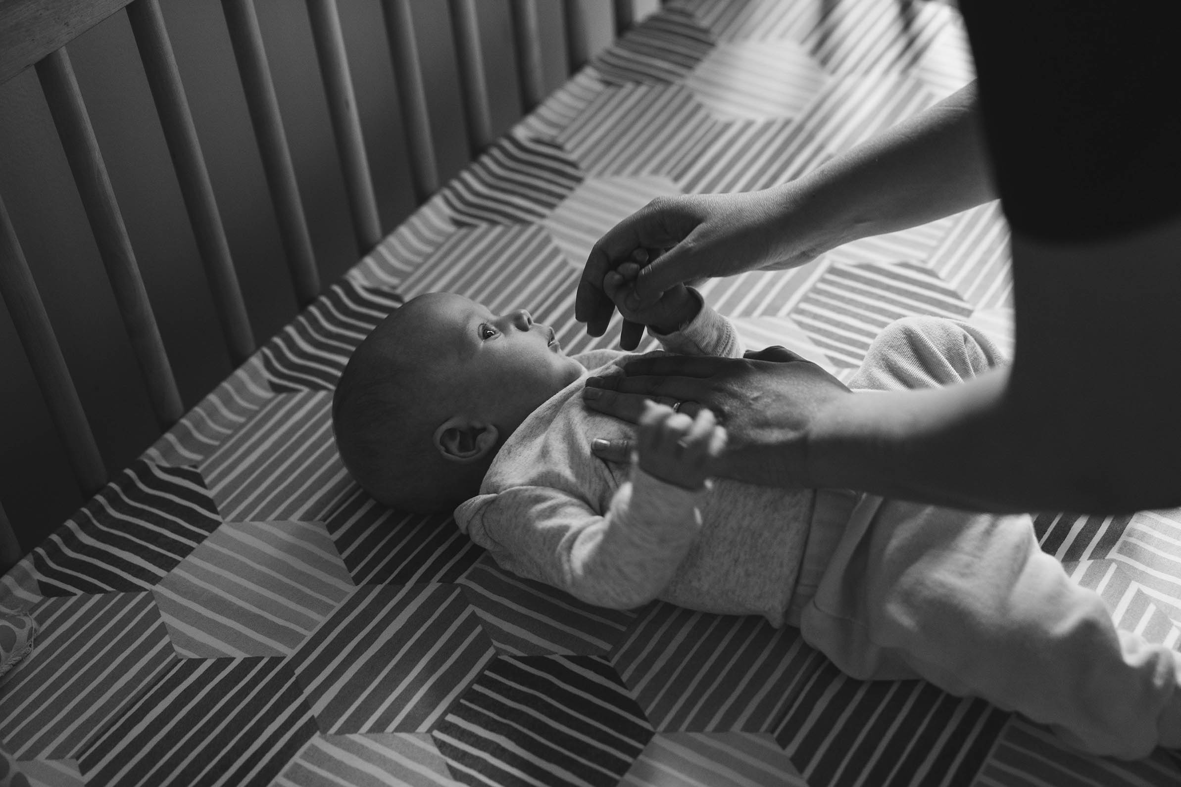 A documentary photograph of a mom putting her baby in the crib during an in home family session