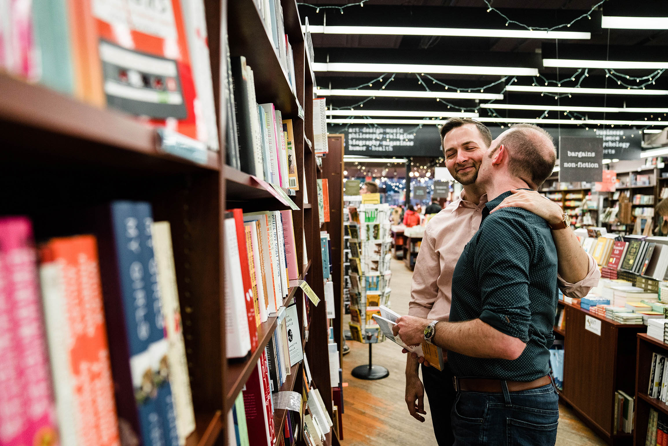 A documentary portrait of a couple hugging and laughing at a bookstore during their Boston engagement session
