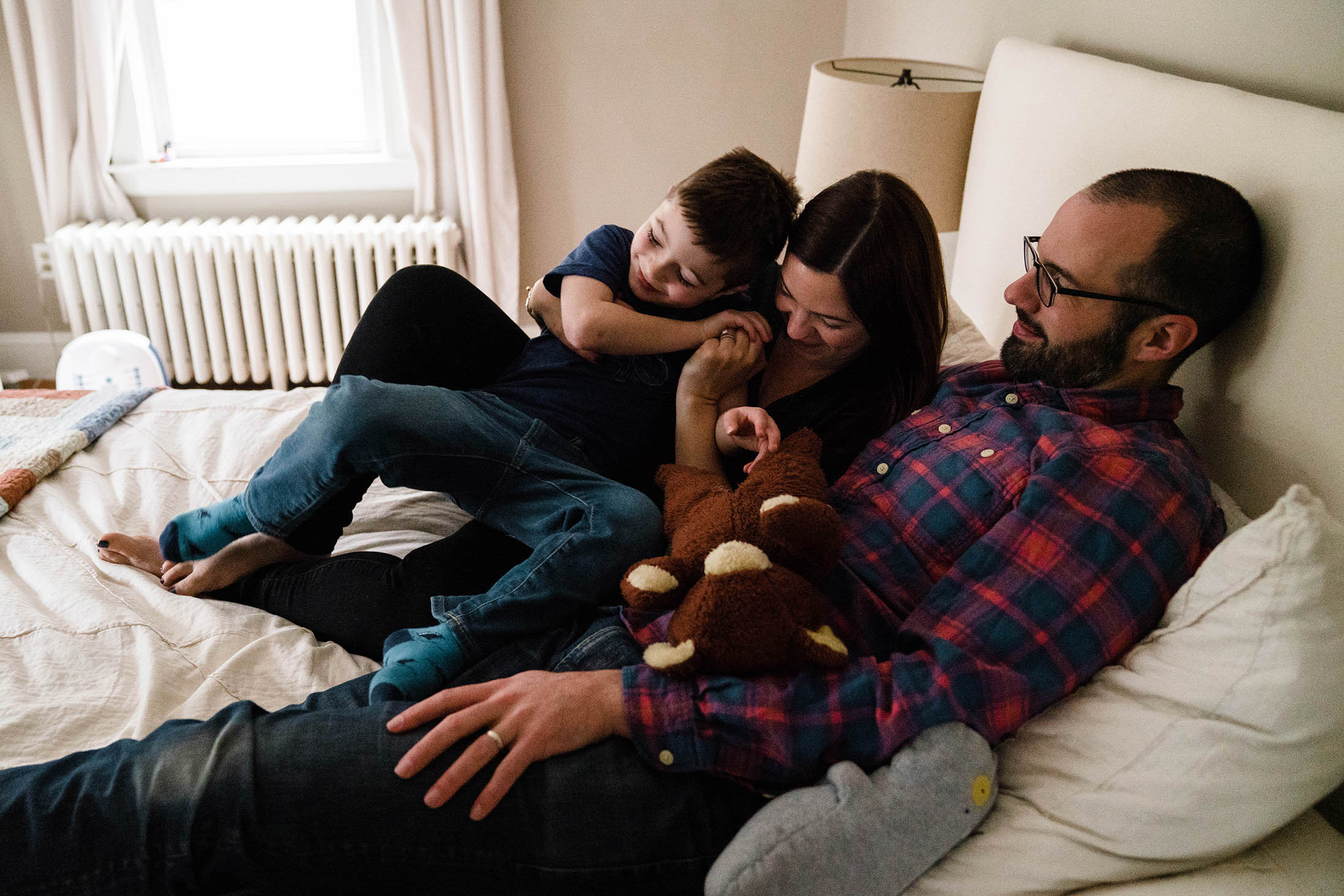 A documentary photograph of a family snuggling in bed during an in home family session in Boston