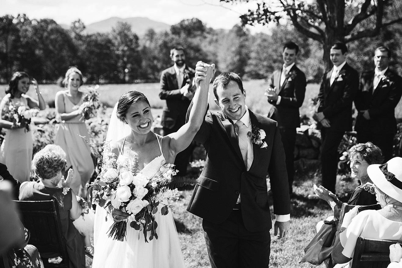 A documentary photograph of a bride and groom celebrating as they walk down the aisle after their moody mountain farm wedding ceremony
