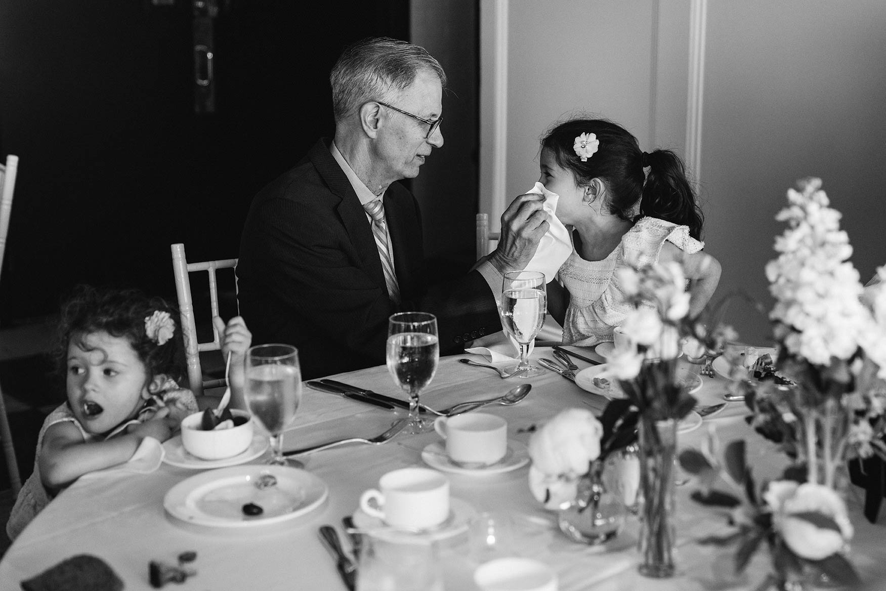 A documentary photograph of a grandfather sitting at the table with two little girls during a Taj Boston Wedding