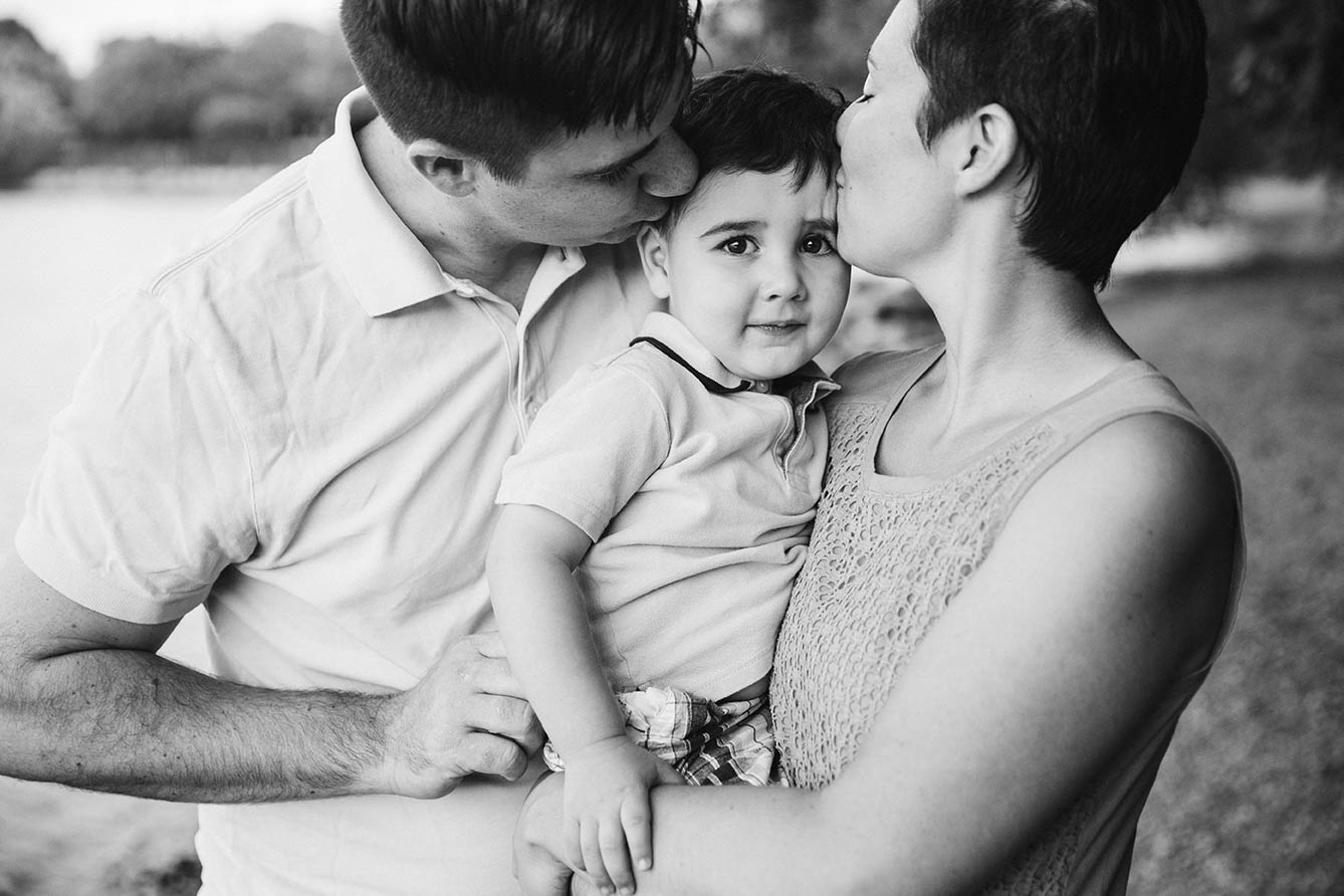 A documentary portrait of parents kissing their son during a family session at Jamaica Pond in Boston