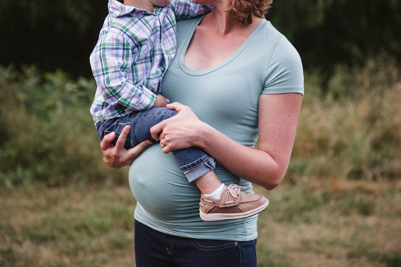 A documentary photograph of a pregnant mom holding her son during their family session at the Arnold Arboretum in Boston