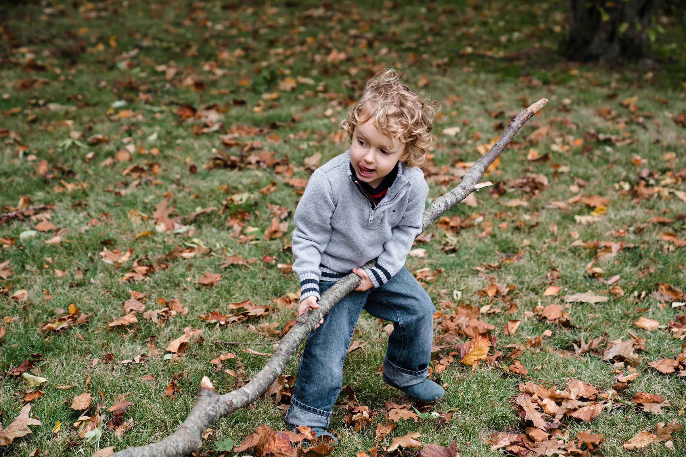 A documentary photograph of a boy pulling a big stick during a family session at Jamaica Pond in Boston
