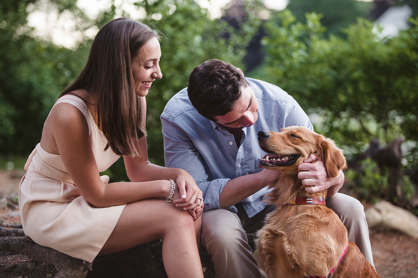 A documentary portrait of a couple petting their dog at Aurburndale Cove during their Boston engagement session