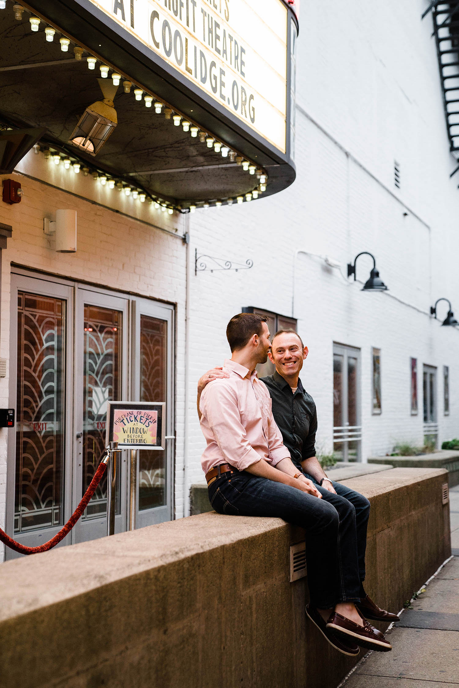 A documentary portrait of a couple sitting outside a movie theater during their Boston engagement session