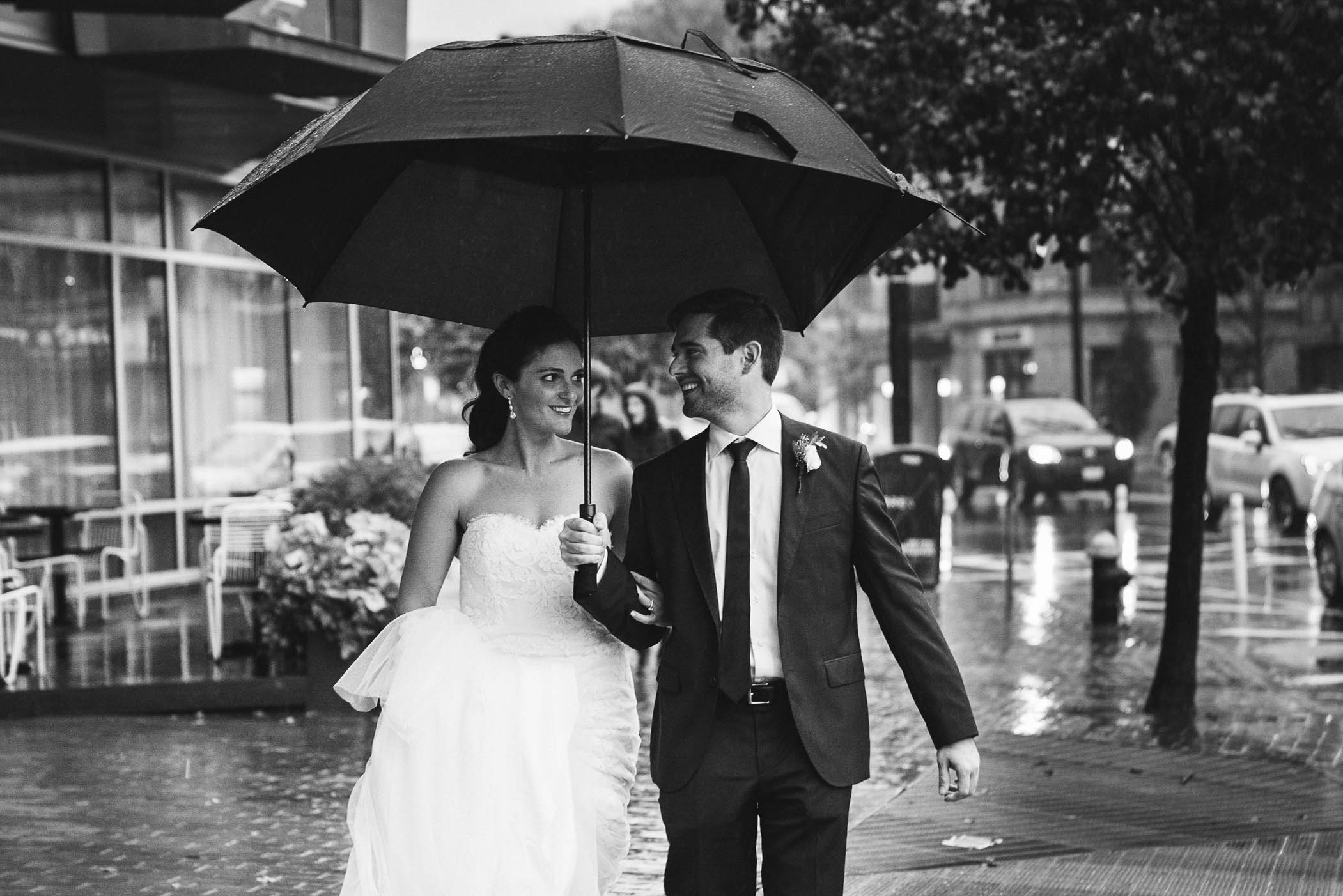 A documentary photograph of a bride and groom walking in the rain during their Cyclorama wedding in Boston's South End