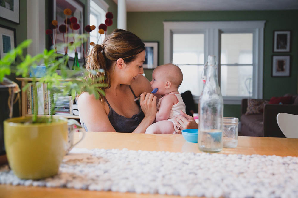 A documentary photograph of a mom feeding her baby during an in home family session in Boston